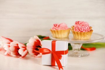 Present box with tulips and cupcakes on blurred background