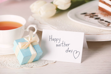 Happy mother day greeting with tulips, cup of tea and present box on wooden table closeup