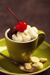 Chocolate cake in a green mug  with whipped cream and a cherry on top, close up