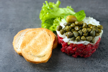 Beef tartare served with a croutons on a grey surface, close up