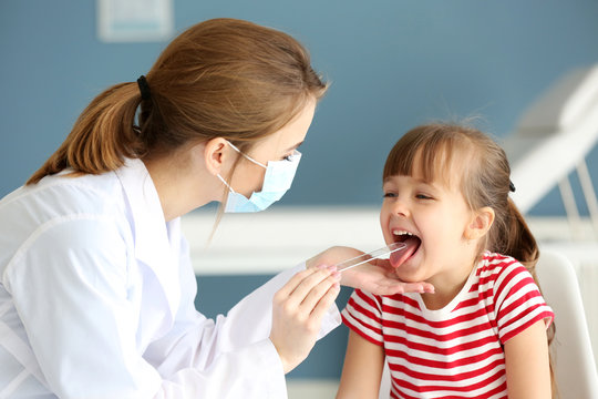 Doctor checking little girl's throat in the office