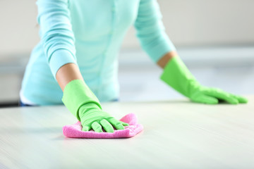 Woman in protective gloves cleaning kitchen table with rag