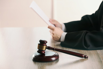 Judge reading document with gavel at wooden table in courtroom