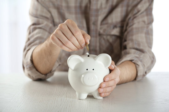 Male hand putting coin into piggy bank at wooden table closeup