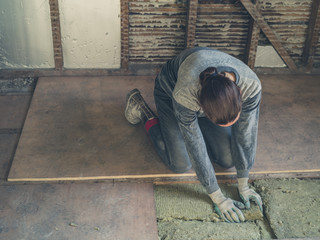 Young woman laying insulation in loft - obrazy, fototapety, plakaty