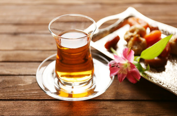 Glass of tea and metal tray with dried fruits on wooden background