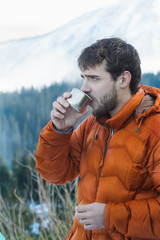 Portrait of resting mountaineer with hot drink metal vacuum flask at snowy mountains background