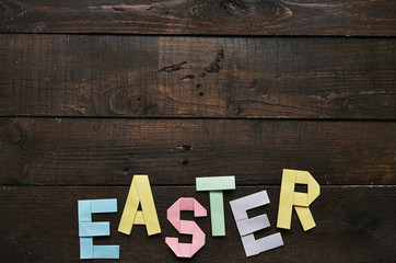 Easter folded paper origami colorful lettering on dark barn wood rustic planks background. Space for text, copy. Holiday greeting postcard template.