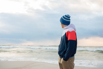 Young man in a hat standing by the sea and looks into the distance