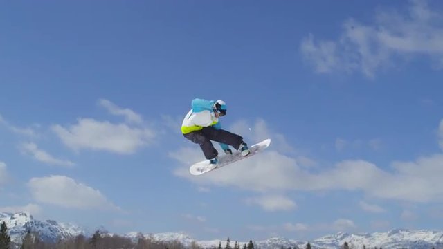 SLOW MOTION CLOSEUP: Snowboarder jumping the kicker in sunny winter