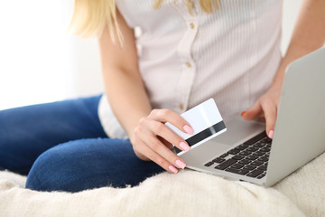 Naklejka premium Happy woman doing online shopping at home . Close- up of a hand holding a credit card next to a laptop