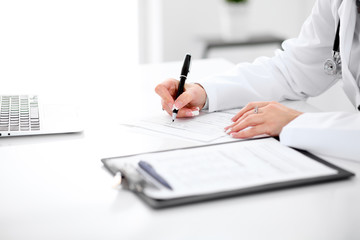 Close-up of a female doctor filling  out application form , sitting at the table in the hospital