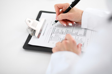 Close-up of a female doctor filling  out application form , sitting at the table in the hospital