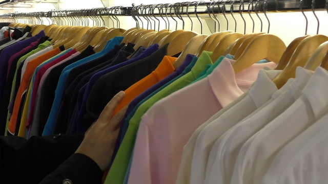 Close up of man hands picking choosing polo shirt from the collection hanging in the store.