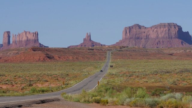 A car passes through scenic Monument Valley