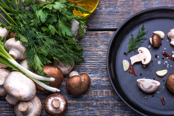 Mushrooms, parsley, dill, onion, olive oil, spices - ingredients for the preparation of mushroom dishes in a frying pan on a wooden background