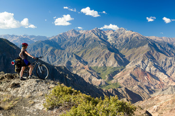 Fototapeta na wymiar Bicycle traveler standing at cliff and enjoying mountain view
