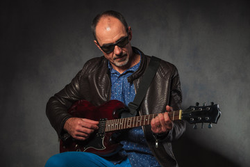 mature man in leather jacket playing guitar