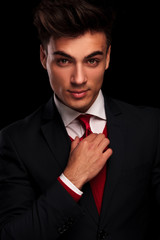 male model in black suit fixing his red tie