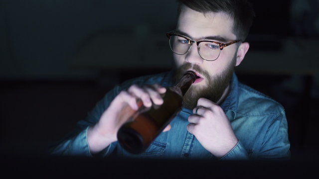 Man drinking beer and using PC at night