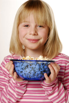 Una niña rubia comiendo palomitas de maíz, sujetando bol con cotufas.