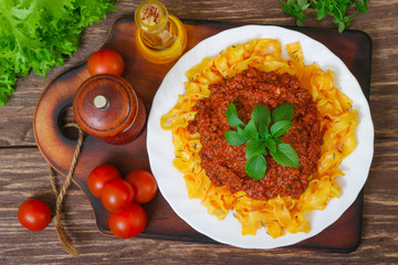 Traditional Italian pasta Bolognese or Bolognese with cooked pasta noodles topped with a spicy tomato based meat sauce garnished with fresh basil on a wooden background