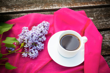Coffee cup and colorful lilac flowers on wooden background