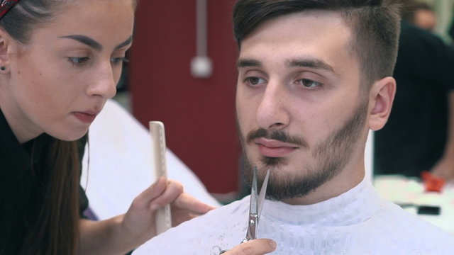Barber cuts the beard of the client with scissors at a barber shop