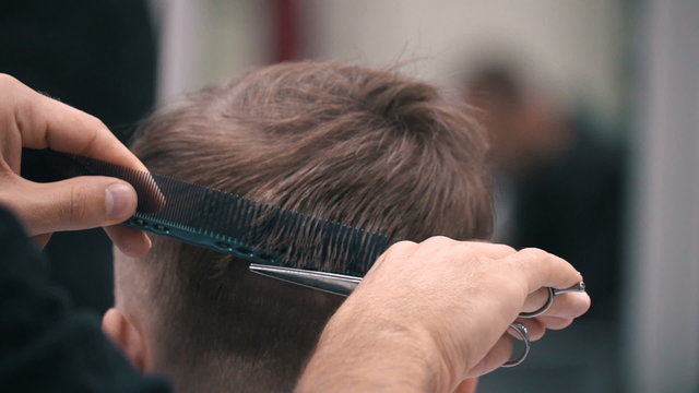 Barber cuts the hair of the client with scissors at a barber shop