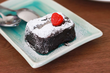 Small piece of chocolate cake with icing sugar and strawberry on top side view, on the square plate on the wood table, Selective focus.