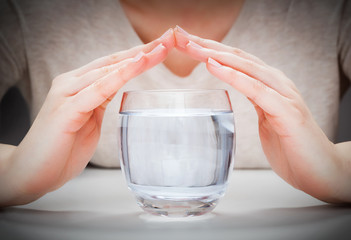 A glass of clean mineral water covered by woman's hands. Environment protection