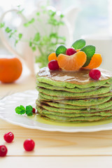 Green pancakes with spinach and bananas decorated citrus, mint and cranberry