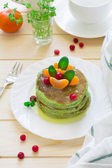 Green pancakes with spinach and bananas decorated citrus, mint and cranberry