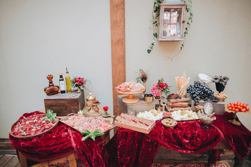 Wedding. Salty bar. Buffet. On the table with a tablecloth color marsala are wooden trays and vases with cheeses, meats, bread, olives and other snacks. in vases lies grapes and tomatoes