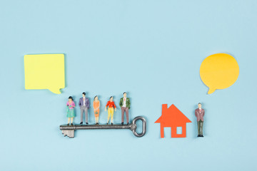 Real Estate concept. Speech bubbles and people toy figures Construction, building. Paper model house with key on blue background. Top view. Copy space for text.