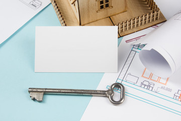 Real estate concept. Silver key with house figure and blank business card on blue background. Top view.