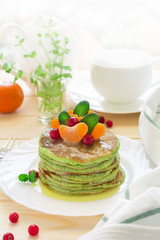 Green pancakes with spinach and bananas decorated citrus, mint and cranberry