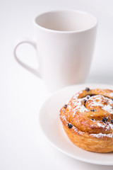 close up of sweet bun with raisins and cup of coffee or tea over