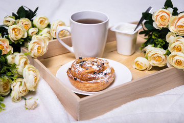 wooden tray with bun, tea, yoghurt and flowers