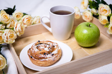 breakfast with bun, apple and tea on wooden tray