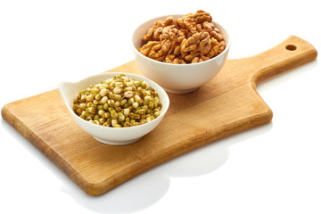 Two bowls with walnuts and mung bean sprouts on wooden board. Isolated on white background.