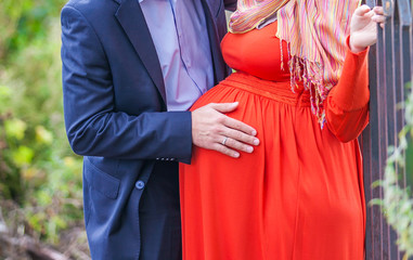 Руки мужчины на животике беременной женщины в красном платье
