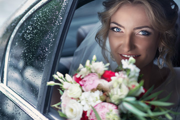 Beautiful blonde bride posing in wedding car on rainy day