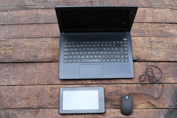 Laptop with digital tablet computer and mouse on old wooden desk 