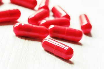 Red pain pills in gelatin capsules on a white wooden background,