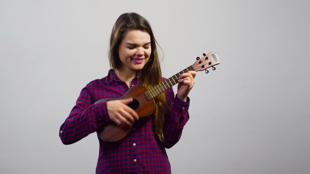 young girl playing ukulele in front of white wall