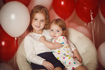 Two little sisters with red and white balloons