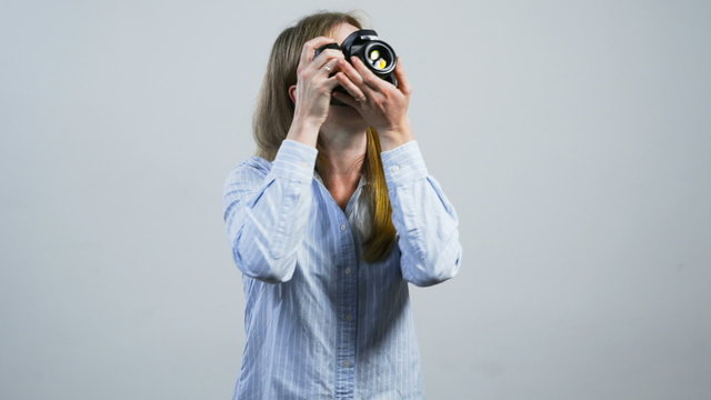 smiling young girl taking pictures with a camera in front of white wall