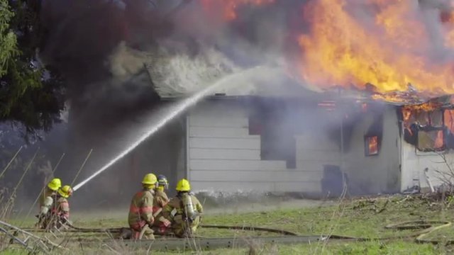 From a safe distance a group of firemen use a hose to spray water over a burning house