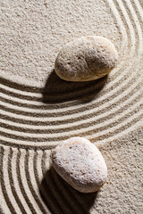 Fototapeta na wymiar zen sand still-life - two stones set across sand lines for concept of spirituality or serenity, top view